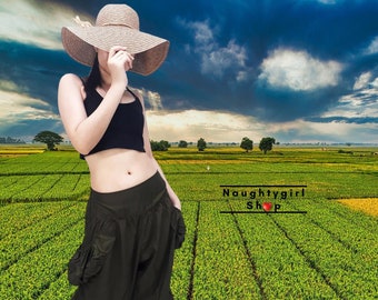 May include: A person wearing a black crop top and dark green, loose-fitting shorts with a large pocket on the side. They are wearing a wide-brimmed straw hat and are standing in a field of green grass. The text "Naughtygirl Shop" is visible in the background.