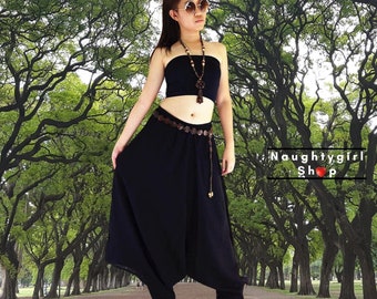 May include: A woman wearing a black strapless top, black harem pants, and a brown beaded belt. She is standing in a grove of trees and is wearing sunglasses.