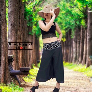 May include: A woman wearing a black crop top with lace detailing, black wide-leg pants with white embroidery, and a straw sun hat. The image includes the text "Naughtygirl Shop".