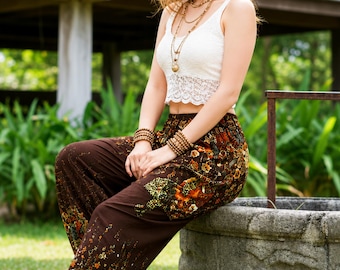 May include: A woman wearing a white lace crop top and brown patterned pants. The pants feature a floral design with orange and green accents. She is also wearing sandals, bracelets, and necklaces.