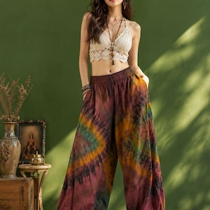 Könnte beinhalten: Ein cremefarbenes Häkel-Crop-Top mit V-Ausschnitt und dünnen Trägern, kombiniert mit einer locker sitzenden Hose mit hoher Taille, die ein Batikmuster in den Farben Kastanienbraun, Senfgelb, Dunkelgrün und Schwarz sowie elastische Beinabschlüsse aufweist.