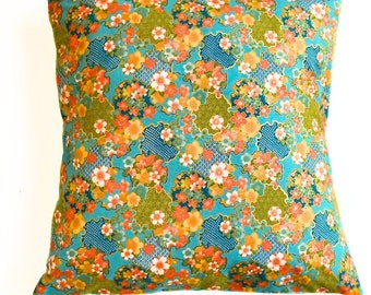 May include: A teal blue throw pillow with a floral pattern featuring orange, pink, and gold flowers. The pillow has a square shape and is made of fabric.