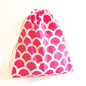May include: A pink drawstring bag with a white mermaid scale pattern.
