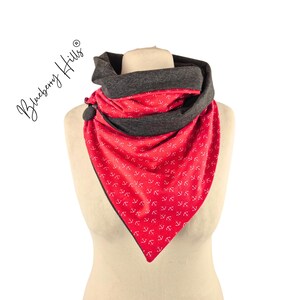 Op de afbeelding: Een rode en grijze sjaal met een ankerpatroon. De sjaal wordt op een mannequin getoond. De tekst "Blueberry Hills" staat in cursief aan de linkerkant van de afbeelding.