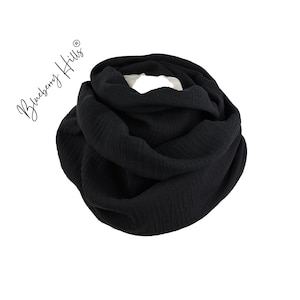 Op de afbeelding: Een zwarte, zachte en textuurrijke oneindige sjaal. De sjaal is gevouwen in een cirkel en is gemaakt van een lichtgewicht stof.