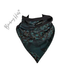 Può includere: Un foulard da collo di colore verde scuro e oro con motivo floreale e bordatura nera. Il foulard è piegato a forma triangolare.