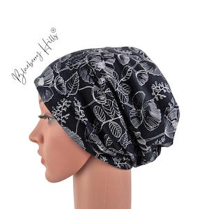 Op de afbeelding: Een zwarte beanie met een wit bloemenpatroon. De hoed is gemaakt van een zacht materiaal en is ontworpen om op het hoofd te worden gedragen. De tekst "Blueberry Hills" staat op de zijkant van de hoed.