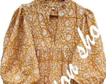 Puede incluir: Un vestido midi de color amarillo mostaza con un estampado floral blanco, cuello alto con volantes y una pequeña abertura frontal, y mangas abullonadas voluminosas con puños elásticos. El vestido tiene una falda escalonada y fluida.