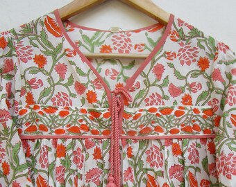 May include: A white cotton tunic with a pink floral print and a pink tassel tie at the neckline.