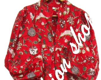 May include: A red midi dress featuring a vibrant floral block print in white, green, and black. The dress has a high ruffled collar, a front button placket, and voluminous puff sleeves with gathered cuffs. The skirt is pleated and falls to a midi length.