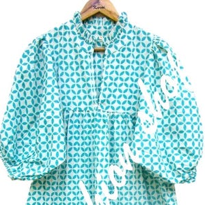 May include: A turquoise blue and white patterned dress with a ruffled neckline and puff sleeves. The dress has a tiered skirt and a white trim around the bottom.