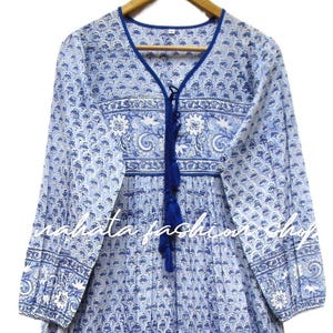 May include: A long-sleeved, blue and white patterned dress with a V-neckline and a tassel tie. The dress features a floral and paisley design, with a flowing skirt and detailed cuffs. The text "mahata fashion shop" is visible.