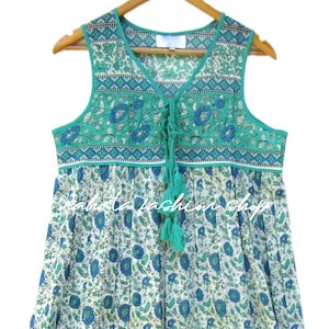 K&ouml;nnte beinhalten: Ein &auml;rmelloses Kleid mit gr&uuml;nem und wei&szlig;em Blumenmuster und einer Schleife am Ausschnitt. Das Kleid hat einen gerafften Rock und einen wei&szlig;en Saum um den Ausschnitt.