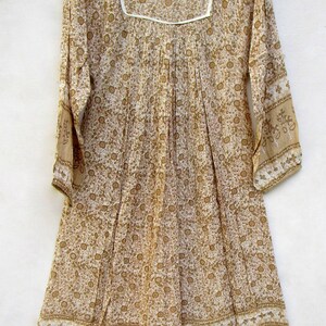 May include: A white cotton dress with a brown floral print and white trim. The dress has long sleeves and a gathered waist.
