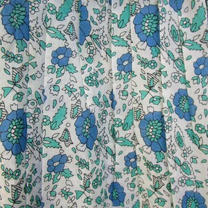 K&ouml;nnte beinhalten: Wei&szlig;er Stoff mit einem blauen und gr&uuml;nen Blumenmuster. Der Stoff ist gefaltet und hat ein zartes, vintage-m&auml;&szlig;iges Aussehen.