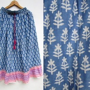 May include: A blue skirt with a white floral pattern and a pink and purple patterned border. The skirt has a drawstring waist with a pink tassel. The fabric appears to be lightweight.