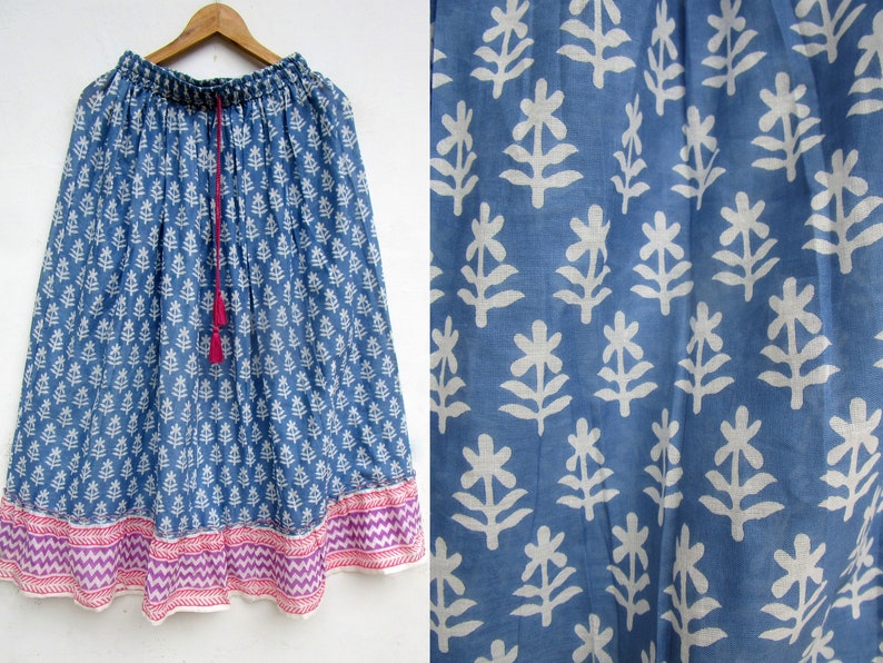 May include: A blue skirt with a white floral pattern and a pink and purple patterned border. The skirt has a drawstring waist with a pink tassel. The fabric appears to be lightweight.