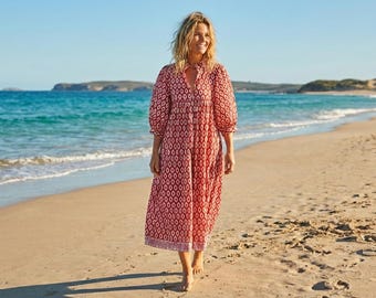 Puede incluir: Un vestido midi con un estampado geométrico de rombos en rojo y blanco, mangas largas abullonadas, escote en V con botones en la parte delantera y una silueta holgada y fluida que llega por debajo de las rodillas.