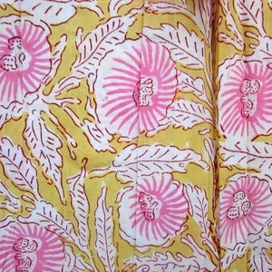 May include: A yellow fabric with a white and pink floral pattern. The flowers have a pink center and white petals with pink outlines. The leaves are white with red outlines.