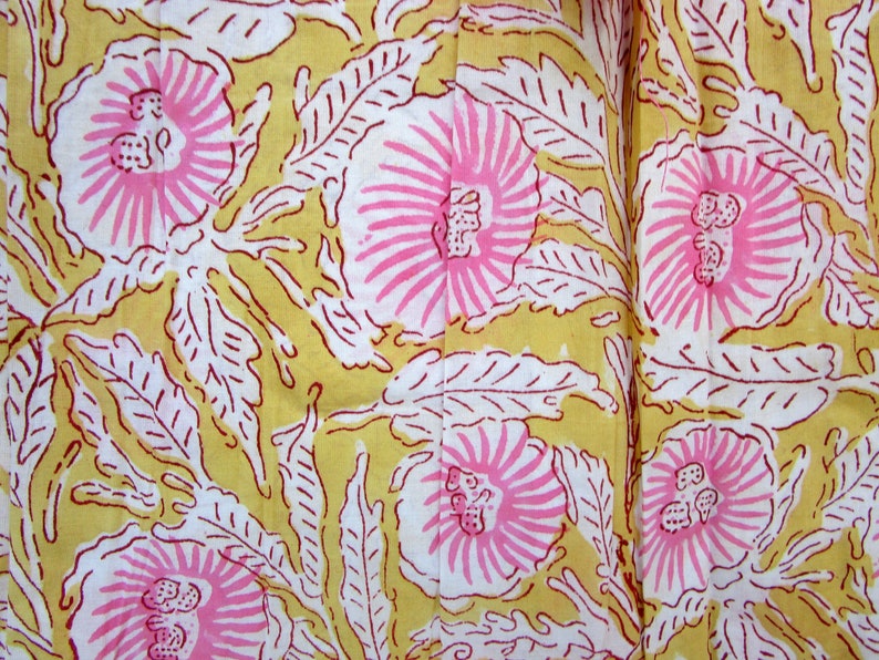 May include: A yellow fabric with a white and pink floral pattern. The flowers have a pink center and white petals with pink outlines. The leaves are white with red outlines.