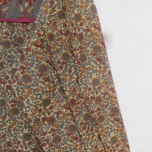 May include: A long-sleeved dress with a floral pattern in shades of beige, brown, red, and gray. The dress features a square neckline with a gray panel and a magenta trim. The fabric appears to be lightweight.