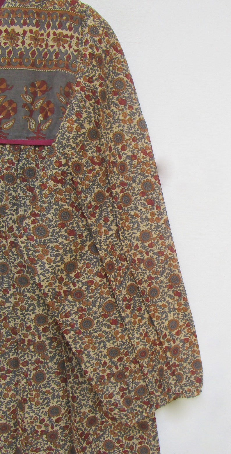 May include: A long-sleeved dress with a floral pattern in shades of beige, brown, red, and gray. The dress features a square neckline with a gray panel and a magenta trim. The fabric appears to be lightweight.