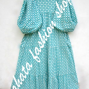 May include: A white and turquoise blue dress with a geometric pattern. The dress has a ruffled neckline and long sleeves. The dress has a tiered skirt and a lace trim at the hem.