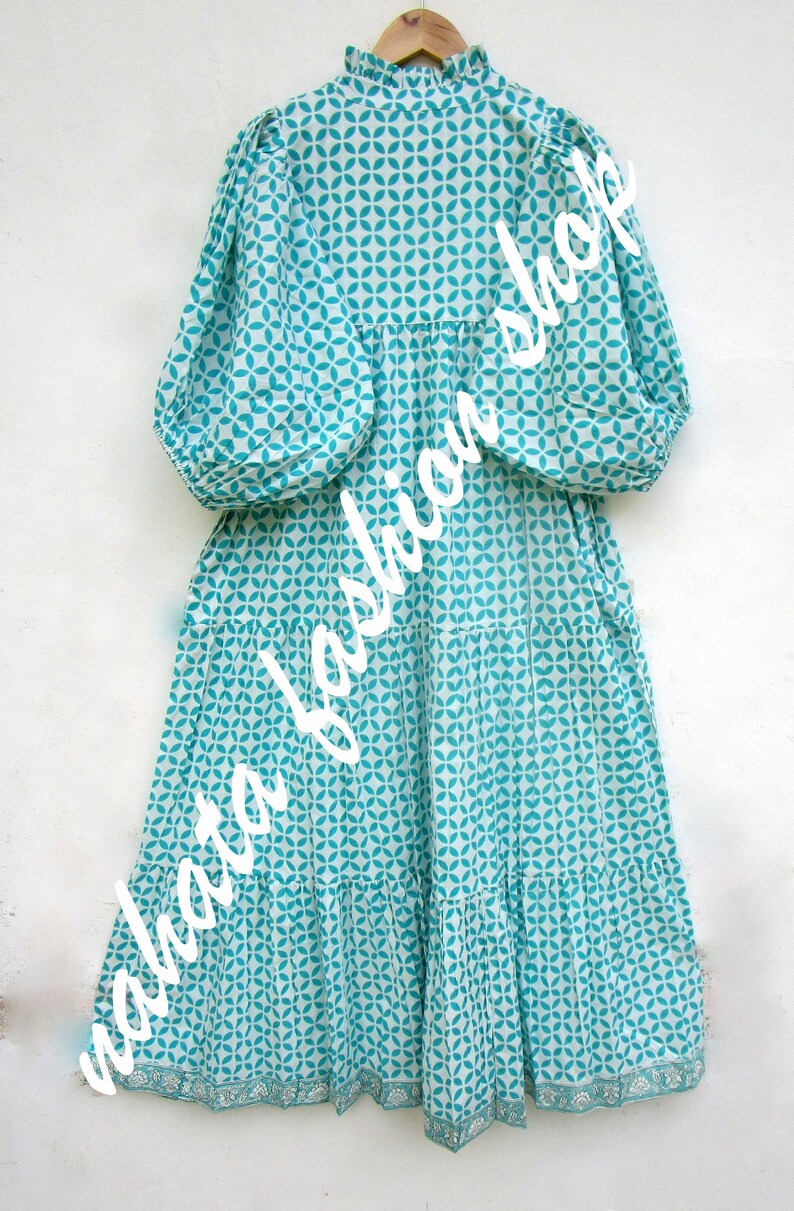 May include: A white and turquoise blue dress with a geometric pattern. The dress has a ruffled neckline and long sleeves. The dress has a tiered skirt and a lace trim at the hem.