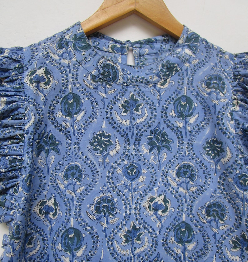 May include: A blue cotton top with a floral print. The top has a round neckline and short sleeves with ruffles.