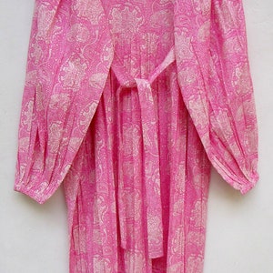 May include: A long, pink dress with a paisley pattern in a lighter pink. The dress has long sleeves, a round neckline, and a matching tie belt. The fabric appears lightweight and flowing, suitable for warm weather.