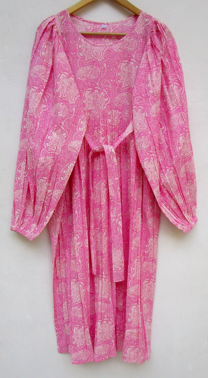 May include: A long, pink dress with a paisley pattern in a lighter pink. The dress has long sleeves, a round neckline, and a matching tie belt. The fabric appears lightweight and flowing, suitable for warm weather.
