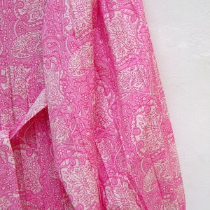 May include: A pink dress with a white paisley pattern. The dress has long sleeves and a tie at the waist. The fabric is lightweight and appears to be cotton or a similar material. The dress is a vibrant pink color.