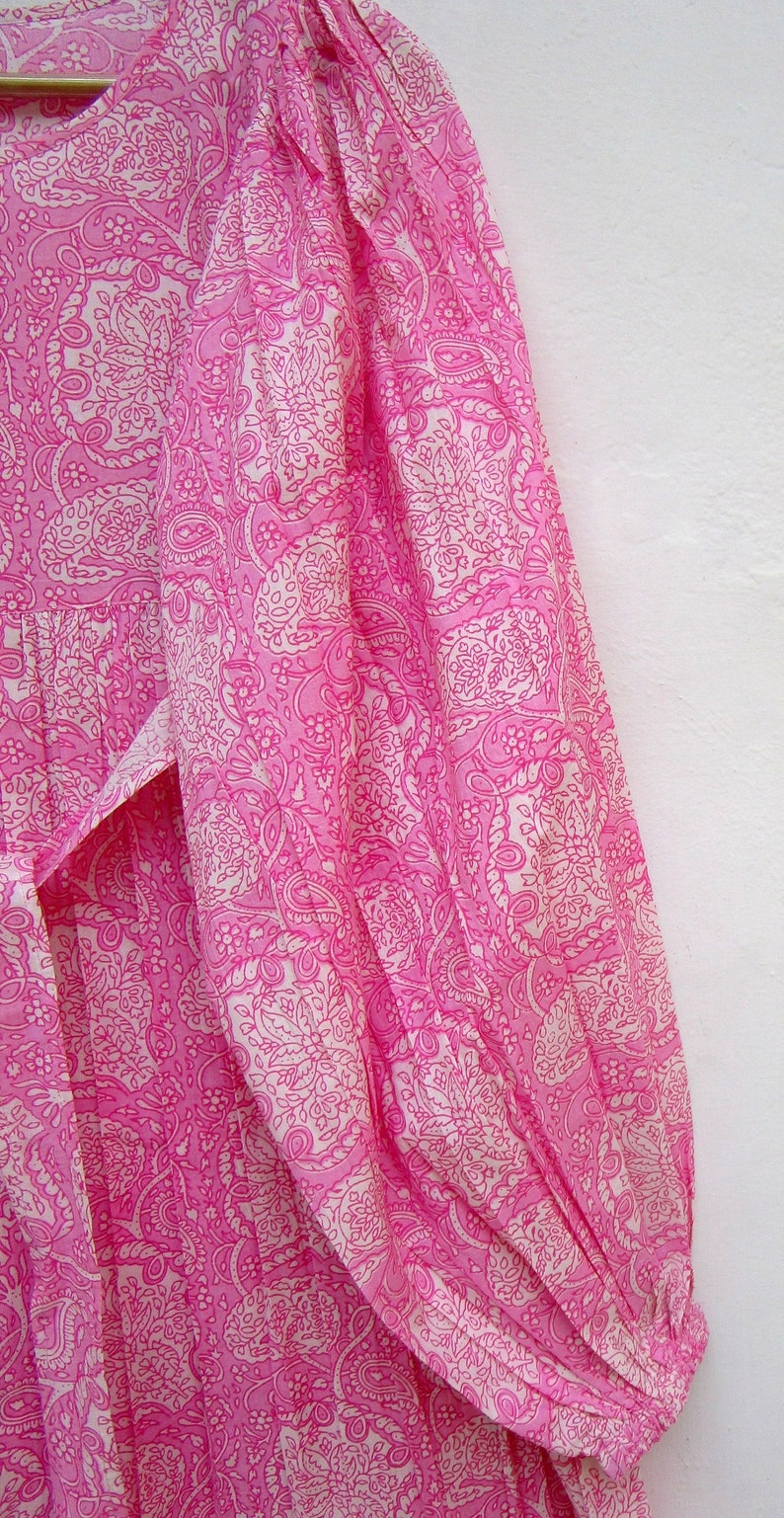 May include: A pink dress with a white paisley pattern. The dress has long sleeves and a tie at the waist. The fabric is lightweight and appears to be cotton or a similar material. The dress is a vibrant pink color.