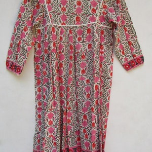 Puede incluir: Un vestido de algod&oacute;n blanco con estampado floral rosa y verde. El vestido tiene un escote redondo, mangas 3/4 y una falda fruncida.