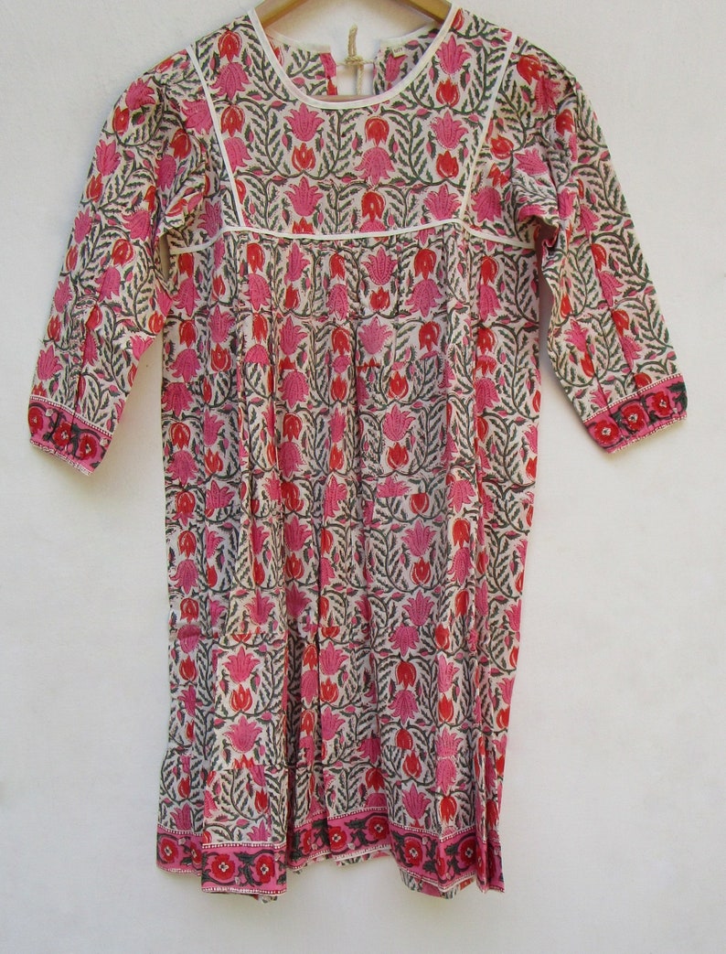 Puede incluir: Un vestido de algod&oacute;n blanco con estampado floral rosa y verde. El vestido tiene un escote redondo, mangas 3/4 y una falda fruncida.