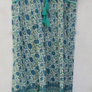 K&ouml;nnte beinhalten: Ein &auml;rmelloses Kleid mit einem Blumendruck in Blau- und Gr&uuml;nt&ouml;nen. Das Kleid hat einen Knoten am Ausschnitt und ein Quasten-Detail.
