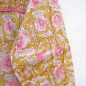 May include: A yellow and pink floral print fabric with a pink trim. The fabric has a traditional Indian design.