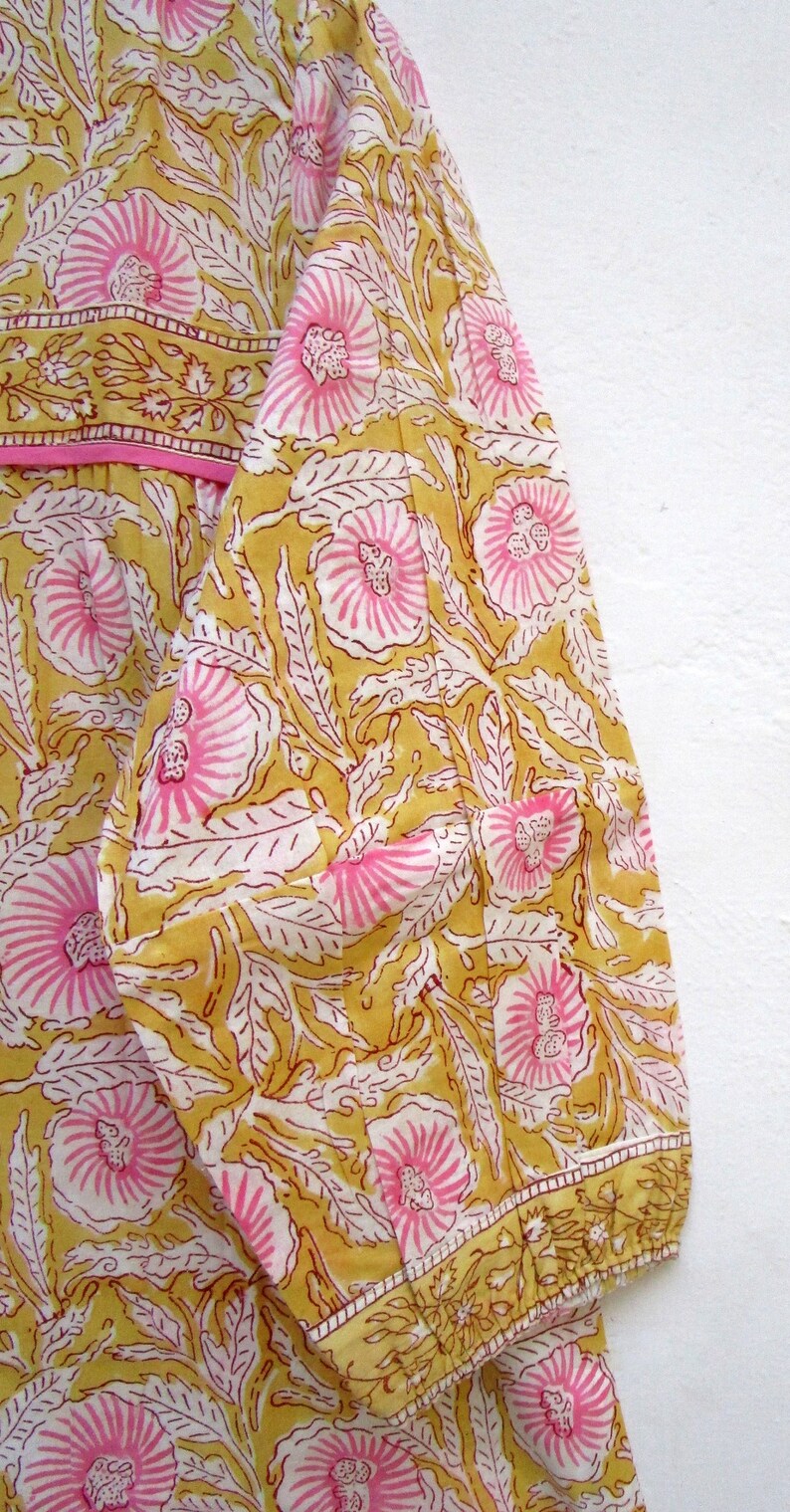 May include: A yellow and pink floral print fabric with a pink trim. The fabric has a traditional Indian design.