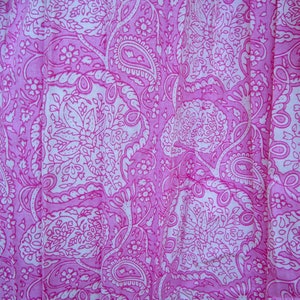 May include: Close-up of a pink fabric with a white paisley pattern. The design features intricate floral and teardrop shapes, creating a detailed and visually appealing textile. The fabric is likely used for clothing or home decor.