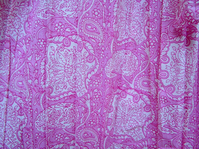 May include: Close-up of a pink fabric with a white paisley pattern. The design features intricate floral and teardrop shapes, creating a detailed and visually appealing textile. The fabric is likely used for clothing or home decor.