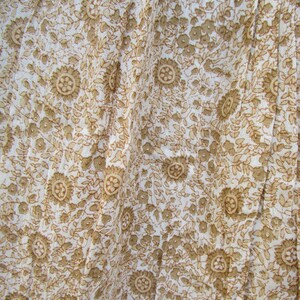 May include: White fabric with a brown floral pattern. The fabric is wrinkled and has a soft, flowing texture.