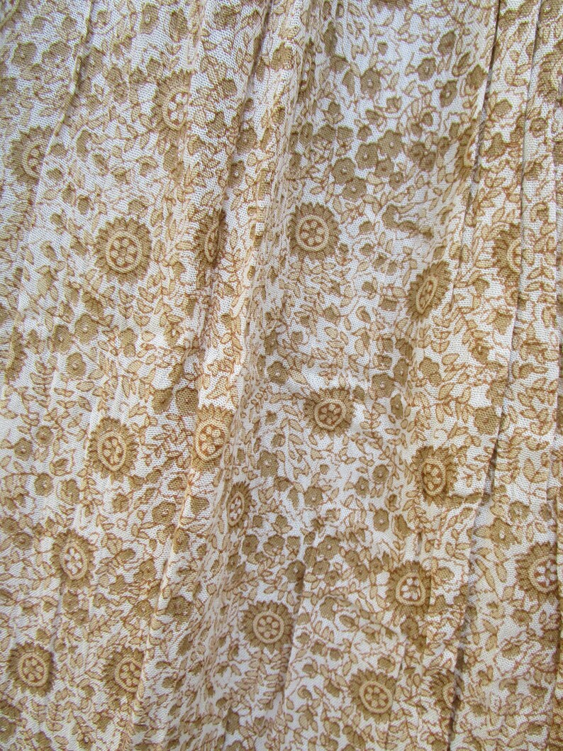 May include: White fabric with a brown floral pattern. The fabric is wrinkled and has a soft, flowing texture.