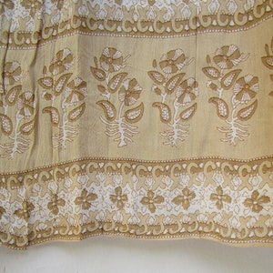 May include: A beige fabric with a white floral pattern. The fabric has a repeating pattern of flowers and leaves. The fabric is trimmed with a white and beige border.
