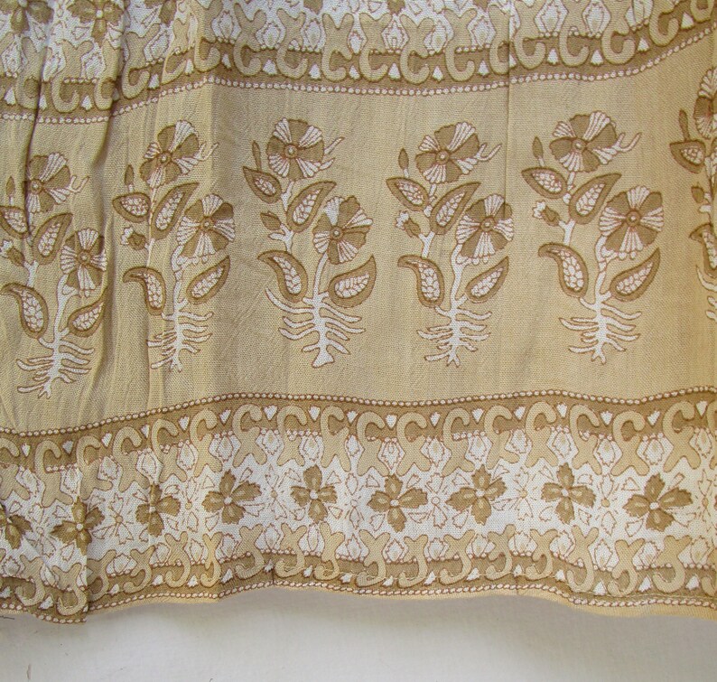 May include: A beige fabric with a white floral pattern. The fabric has a repeating pattern of flowers and leaves. The fabric is trimmed with a white and beige border.