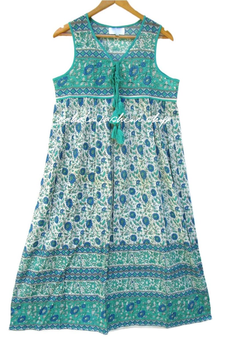K&ouml;nnte beinhalten: Ein &auml;rmelloses Kleid mit gr&uuml;nem und wei&szlig;em Blumenmuster und einer Schleife am Ausschnitt. Das Kleid hat einen gerafften Rock und einen wei&szlig;en Saum um den Ausschnitt.
