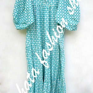 May include: A white and turquoise blue cotton dress with a geometric pattern. The dress has a ruffled neckline, 3/4 sleeves, and a tiered skirt.