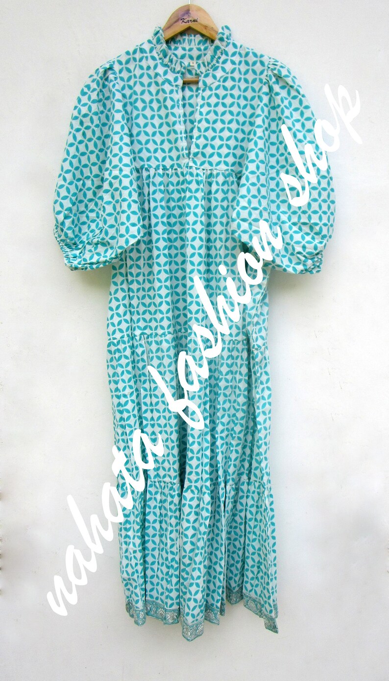 May include: A white and turquoise blue cotton dress with a geometric pattern. The dress has a ruffled neckline, 3/4 sleeves, and a tiered skirt.