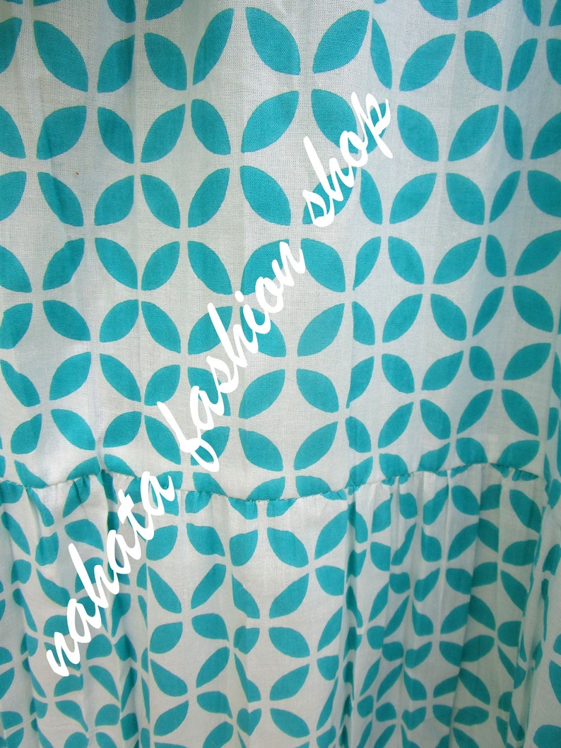 May include: White fabric with a teal blue geometric pattern of overlapping leaf shapes. The fabric has a gathered look at the bottom.