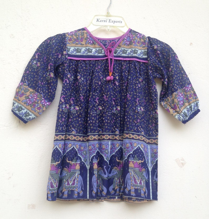 May include: A navy blue tunic top with a floral and elephant print design. The top has three-quarter sleeves, a V-neck with a drawstring, and decorative trim. The brand name "Karni Exports" is visible on the hanger.