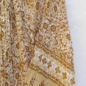 May include: A white cotton dress with a brown floral print. The dress has a white collar and long sleeves with a brown floral print border.